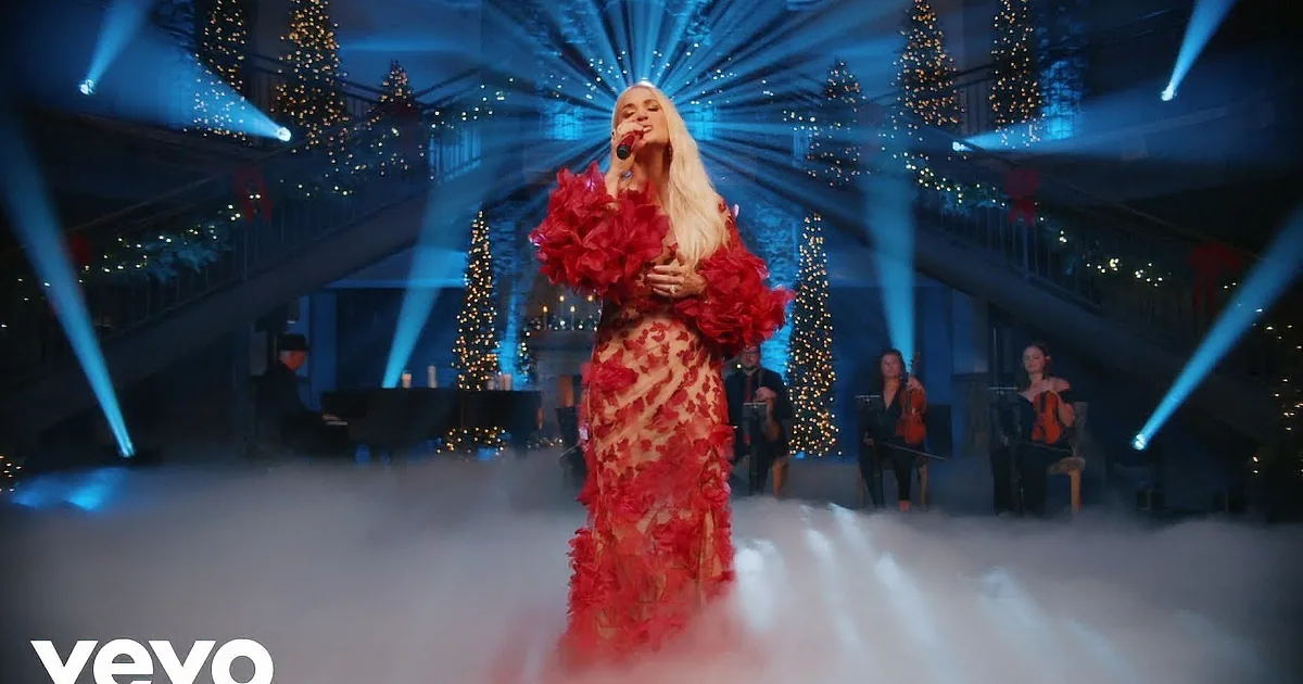 A woman in a red floral dress sings on stage, surrounded by mist and musicians, with Christmas lights in the background.