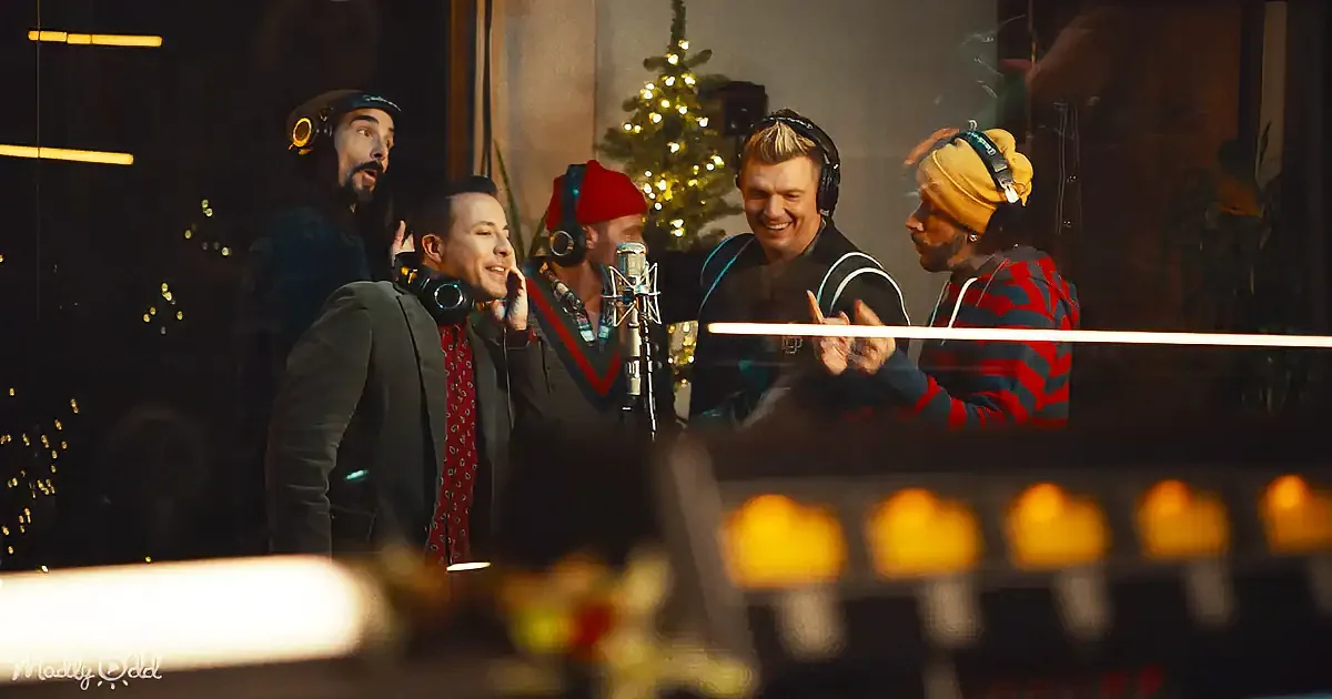 A group of five people in a recording studio, wearing headphones, with a Christmas tree in the background.