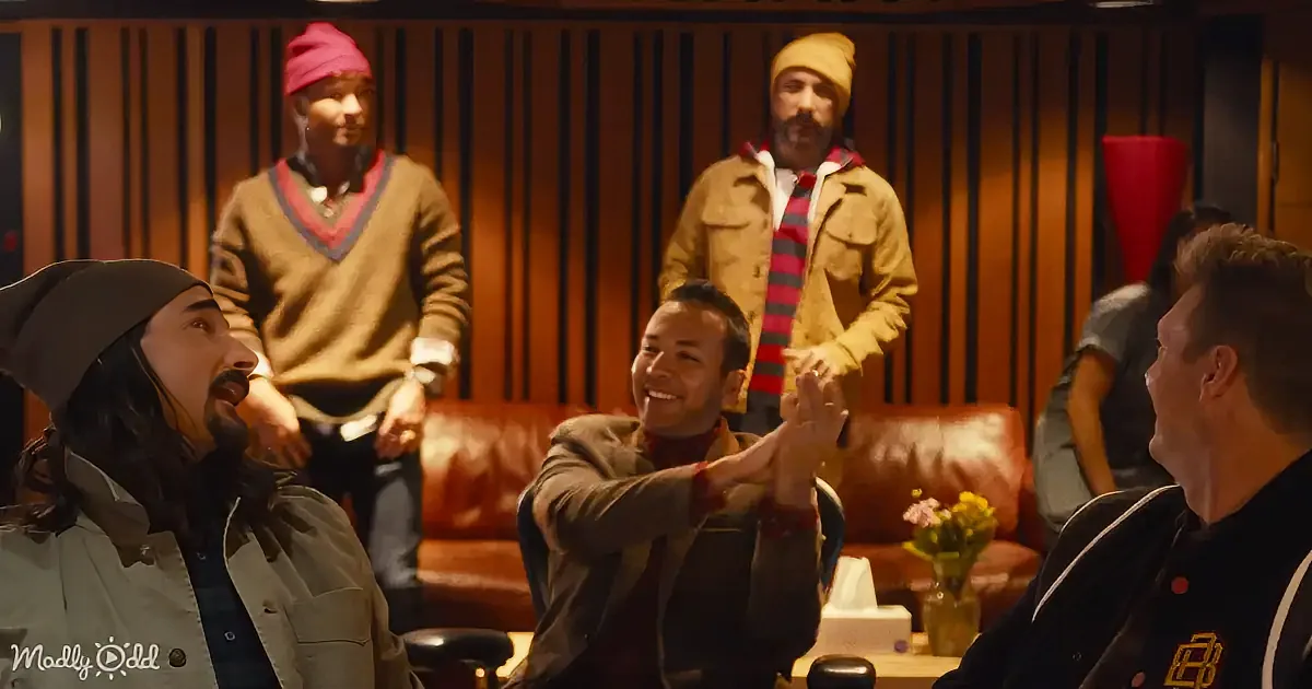A man in a beanie and jacket is clapping, surrounded by others in a warmly lit room with wood paneling.