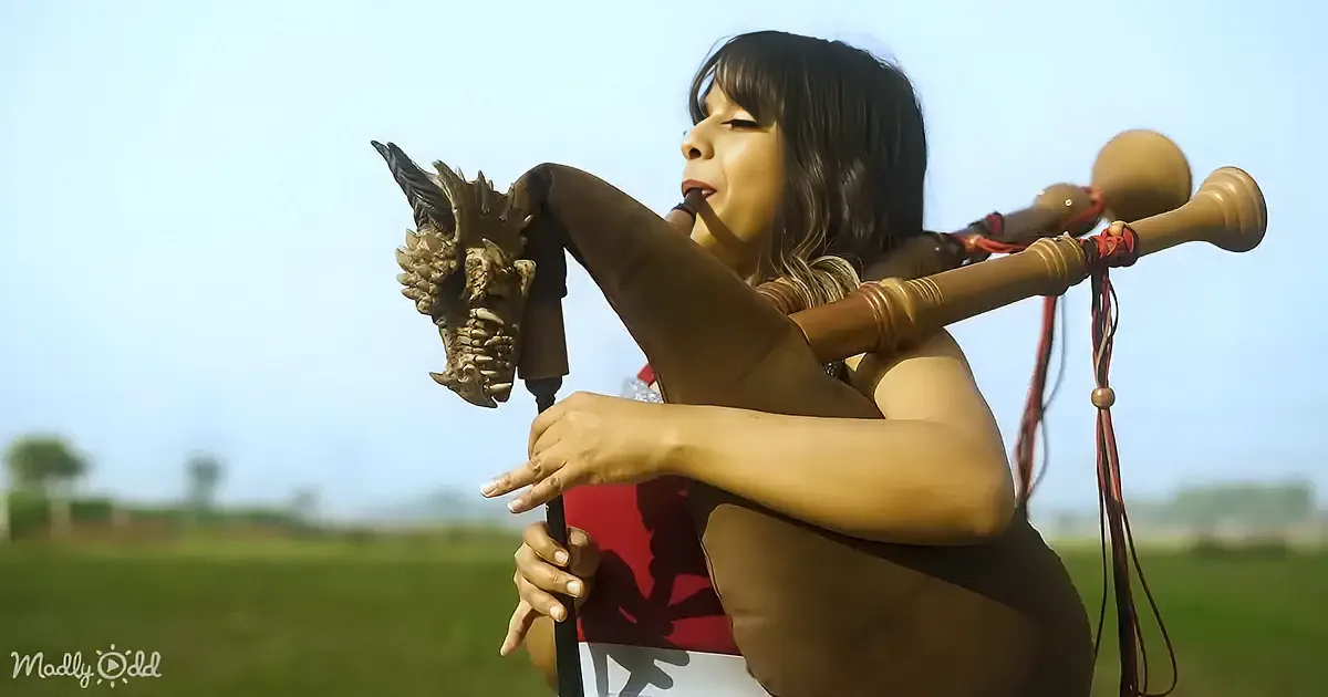 A person holds a dragon-headed flute and another instrument, standing outdoors in a grassy field.