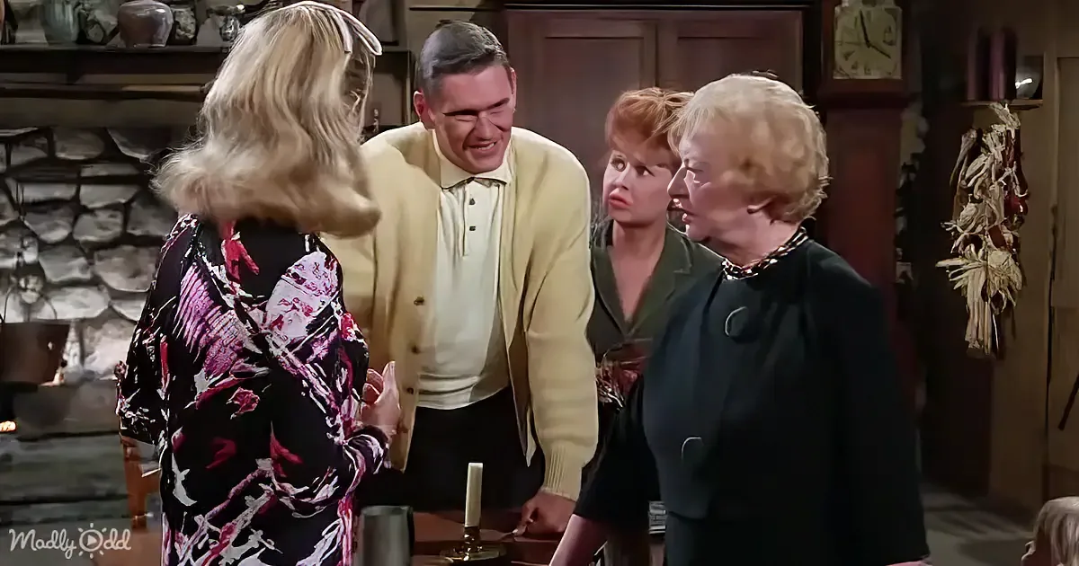 A man in a yellow sweater leans forward, engaging with a woman in a floral dress in a cozy, rustic room.