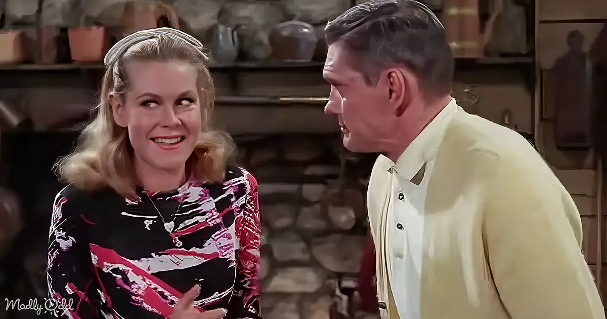 A woman in a patterned top smiles while talking to a man in a light yellow suit in a rustic setting.