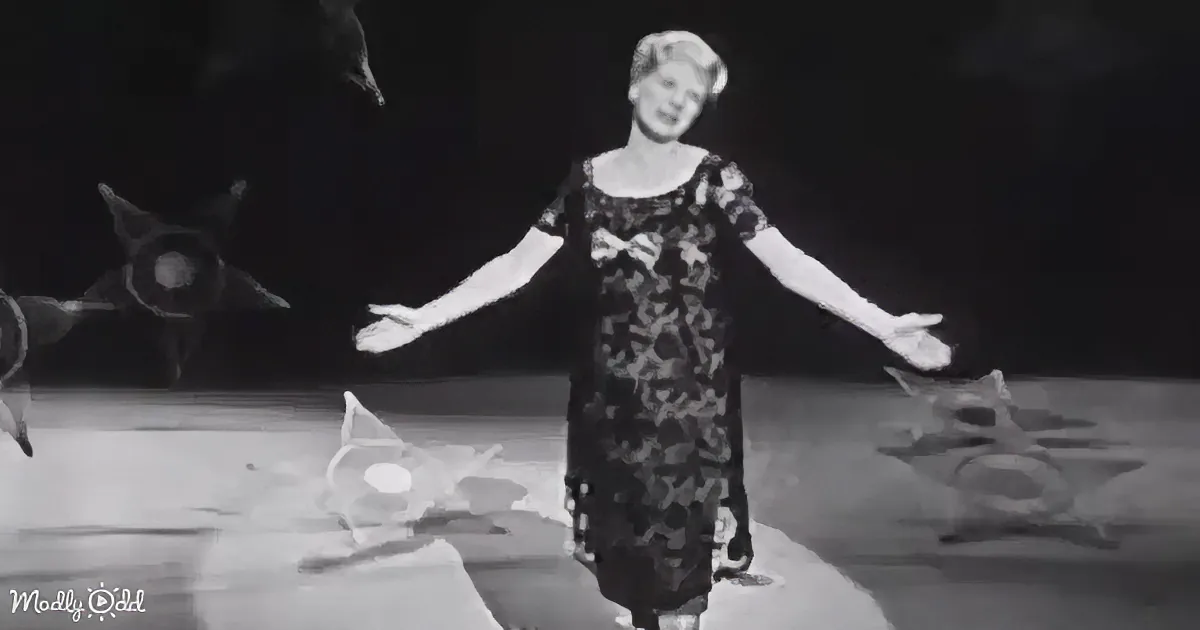 A woman in a patterned dress stands with arms outstretched, surrounded by abstract shapes on a dark stage.