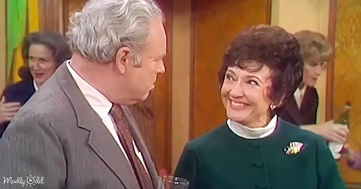 A man in a suit and a woman in a green dress are smiling and talking, surrounded by other people.