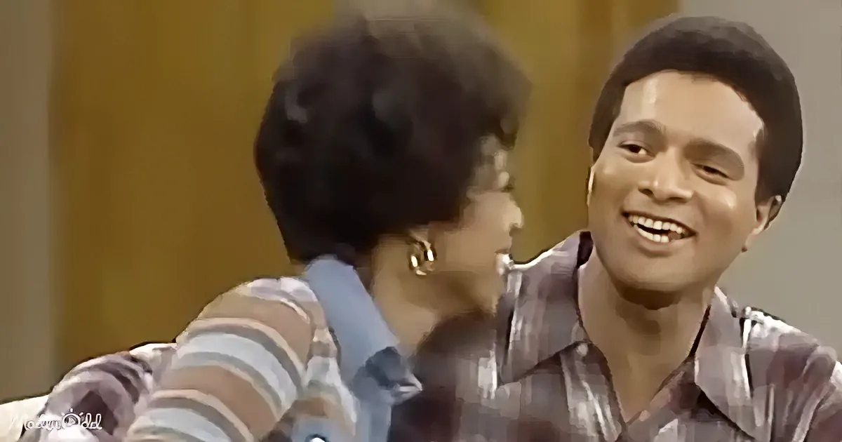 A man in a striped shirt smiles while interacting with a woman in a blue top, both seated and facing each other.