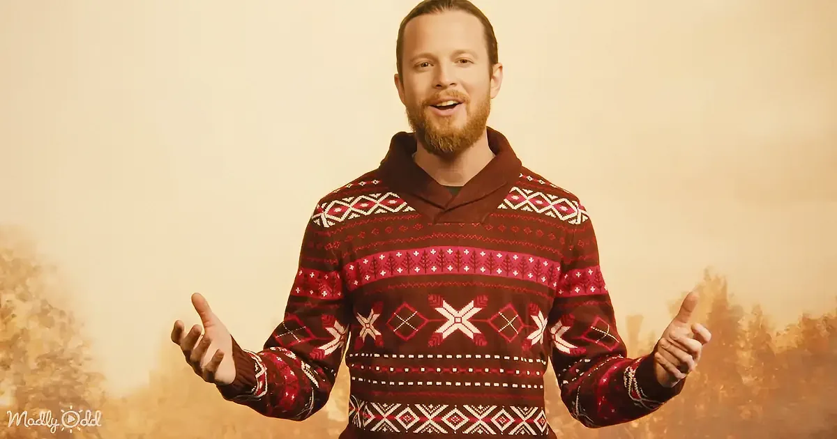 A man in a festive sweater gestures with his hands against a warm-toned background.