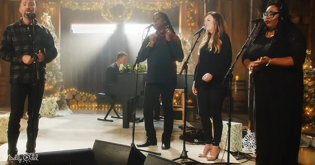 A group of four people singing in front of microphones, decorated with Christmas lights and wreaths.