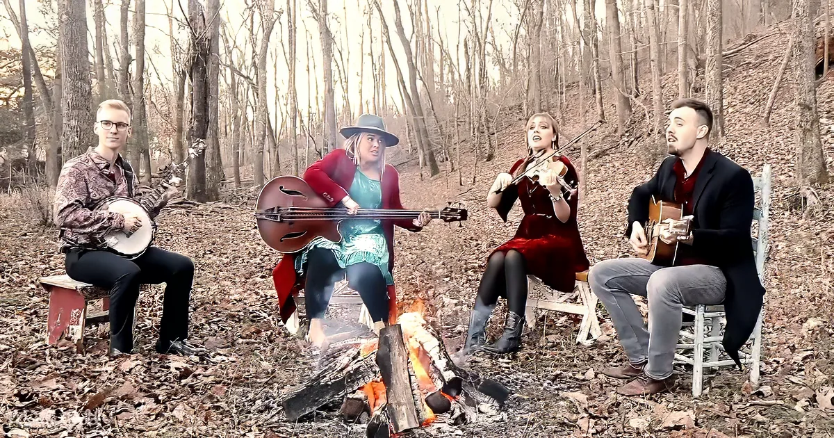 Four musicians play instruments around a campfire in a forest setting.