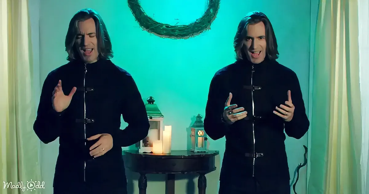 Two identical men in black outfits with long hair stand in front of a teal-lit background, gesturing with their hands.