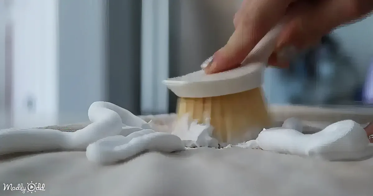 A hand holds a brush, applying a white substance onto a textured surface.