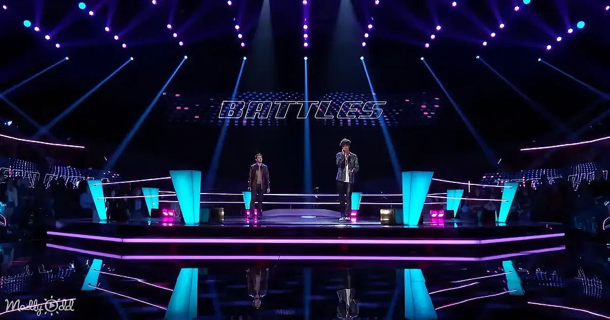 Two individuals stand on a brightly lit stage with "BATTLES" text above, surrounded by vibrant stage lights.