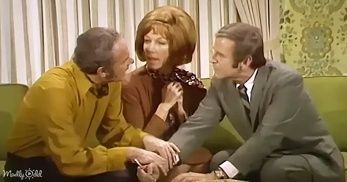 Three individuals in a room, two men leaning in towards a woman, suggesting a tense or intimate moment.