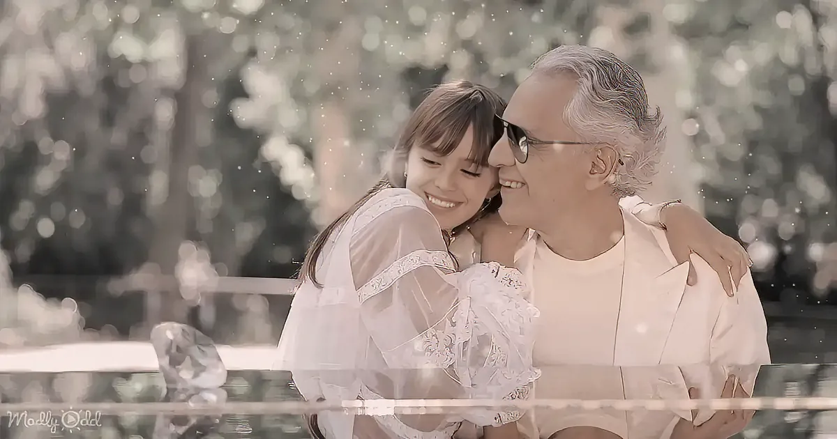 A smiling girl hugs an older man in a serene outdoor setting with blurred greenery.