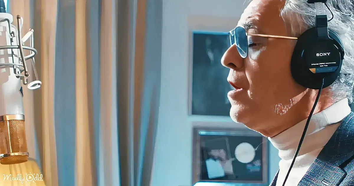An older man wearing headphones and sunglasses is in a recording studio, speaking into a microphone.