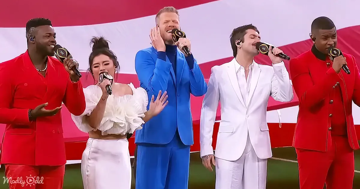 A group of five performers in vibrant outfits sing into microphones, with a red and white striped backdrop.