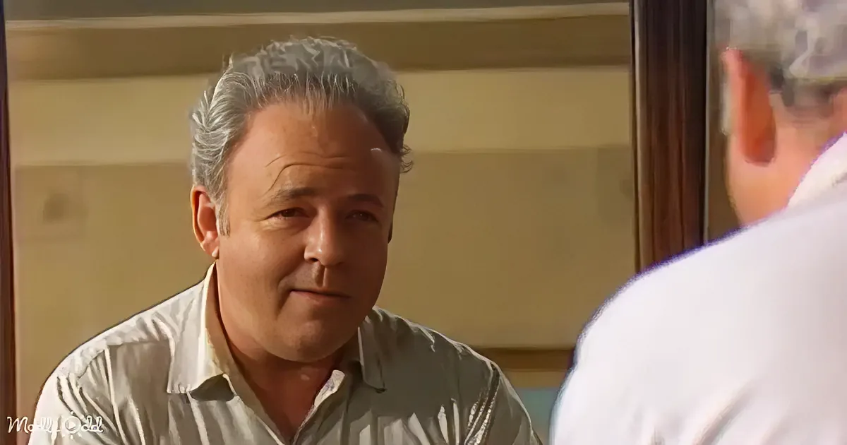 A man with gray hair and a white shirt is seated, looking to his right with a calm expression.