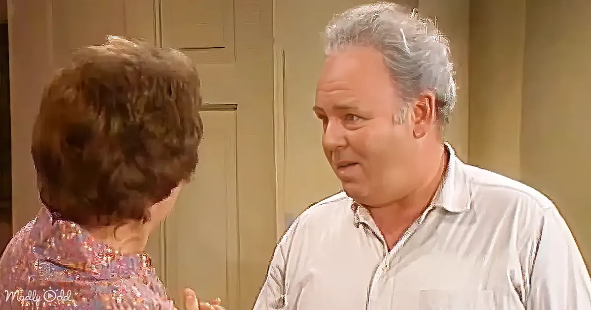 An older man in a white shirt looks concerned while talking to a woman with short brown hair.