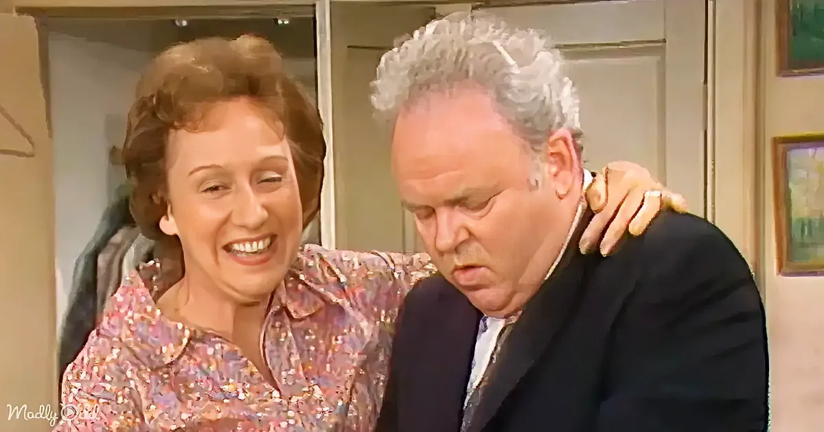A woman in a floral shirt is laughing, with her arm around a man in a suit who looks concerned.