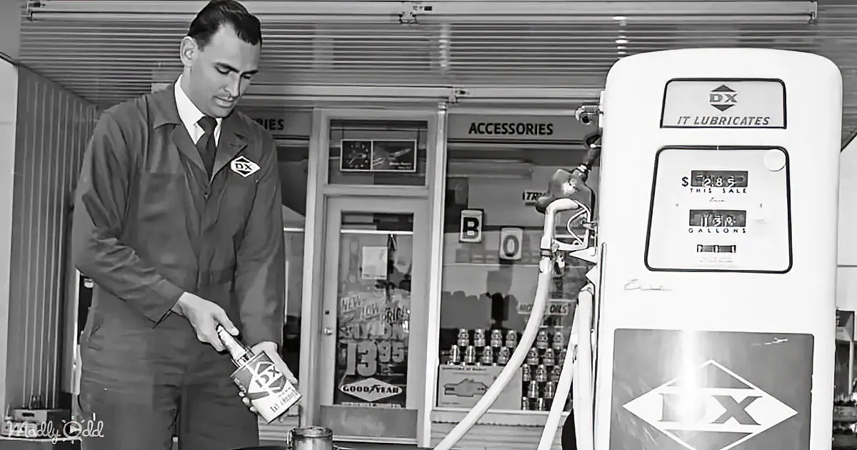 A man in a uniform holds a can near a vintage gas pump at a DX station.