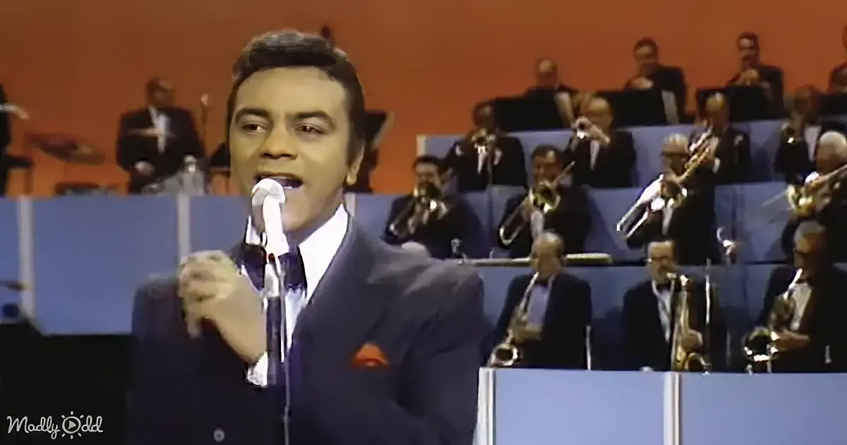 A man in a suit sings into a microphone, surrounded by a band playing brass instruments.