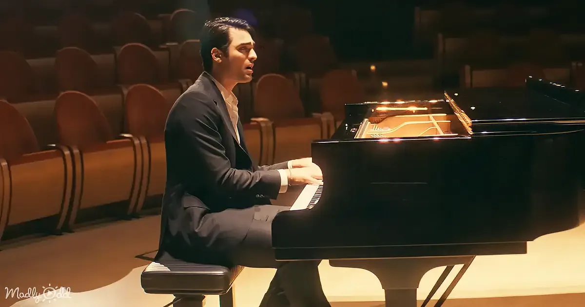 A man in a suit sings while playing a grand piano in an empty auditorium.