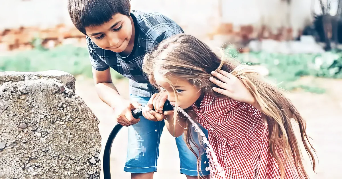 A boy and girl playfully splash water on each other with a hose.