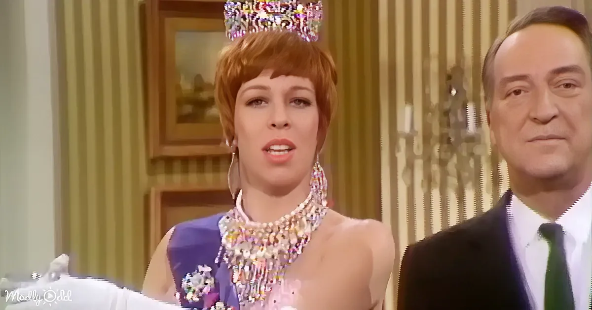 A woman in a tiara and elaborate dress stands next to a man in a suit, both in a formal setting.