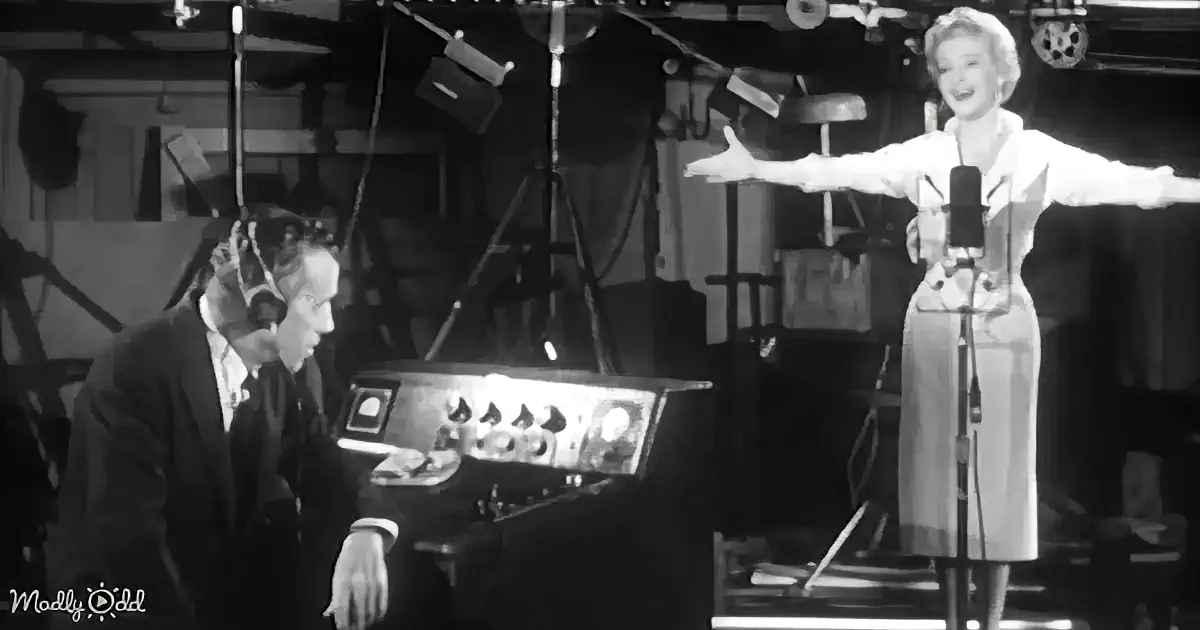 A woman sings into a microphone while a man listens through headphones in a recording studio.