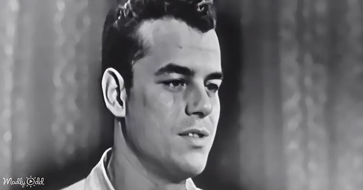 A man with short, dark hair and a white shirt, looking to the side in a black-and-white image.