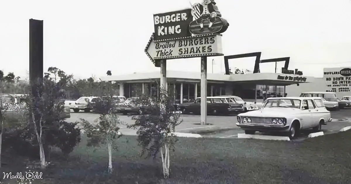 A vintage Burger King sign advertises broiled burgers and thick shakes, with cars parked in front and trees in the...