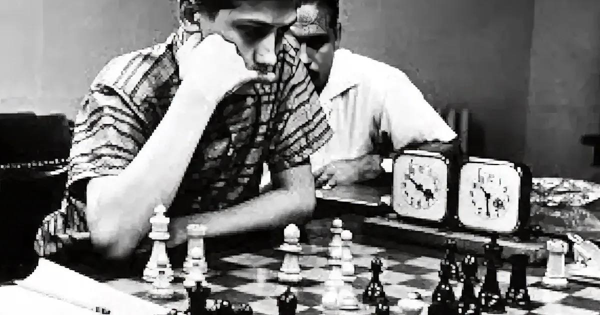A man in a striped shirt is deeply focused on a chess game, leaning over the board.
