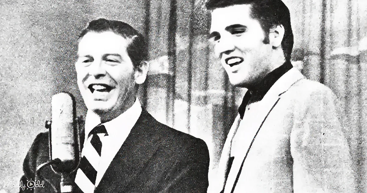 Two men in suits sing into a microphone, one with a striped tie, against a curtain backdrop.
