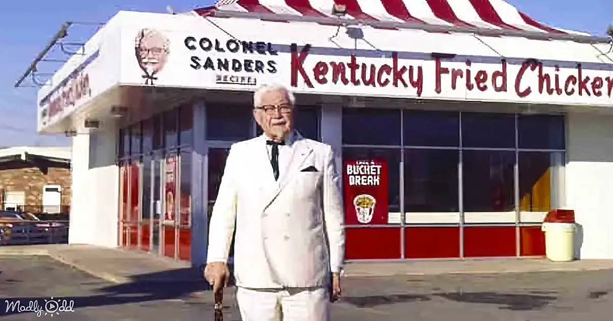 An older man in a white suit stands in front of a Kentucky Fried Chicken restaurant.