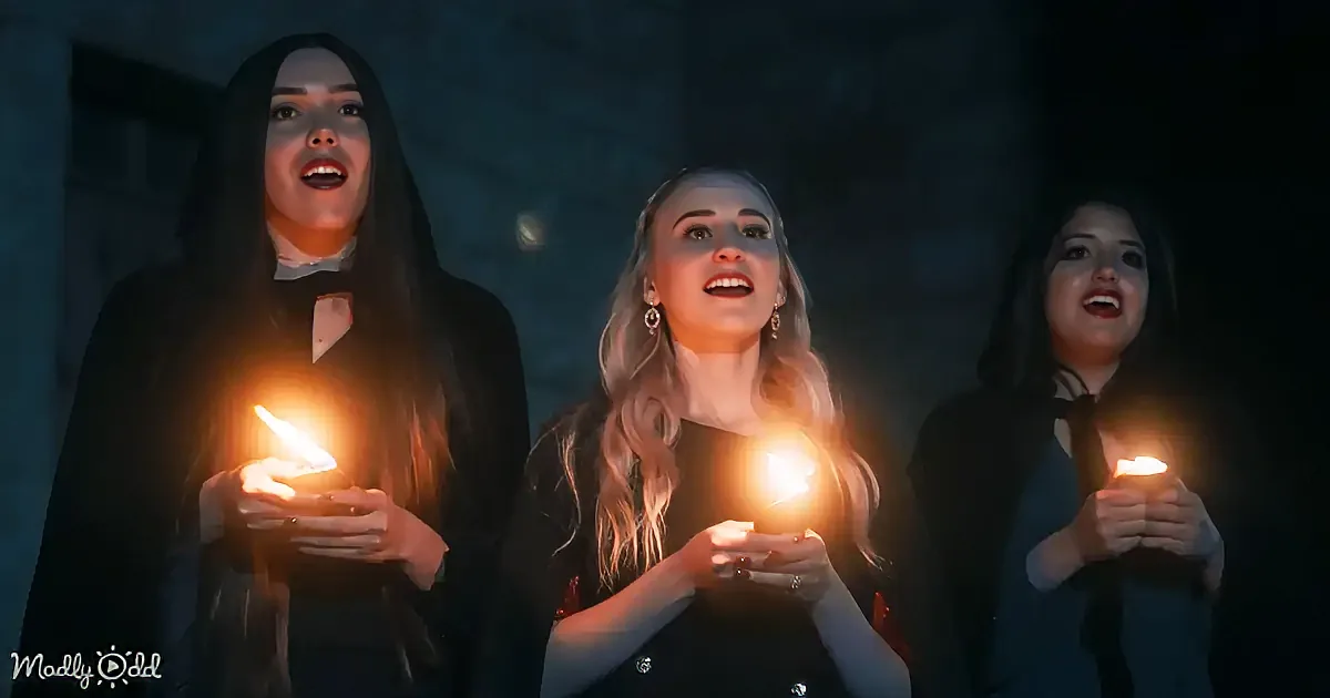 Three women in dark attire hold glowing candles, their faces illuminated, standing against a dark background.