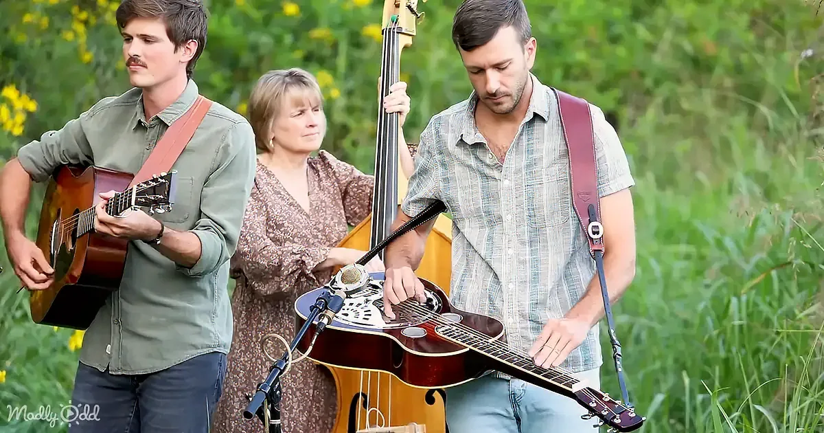 A man plays a guitar while another holds a bass in a grassy field.