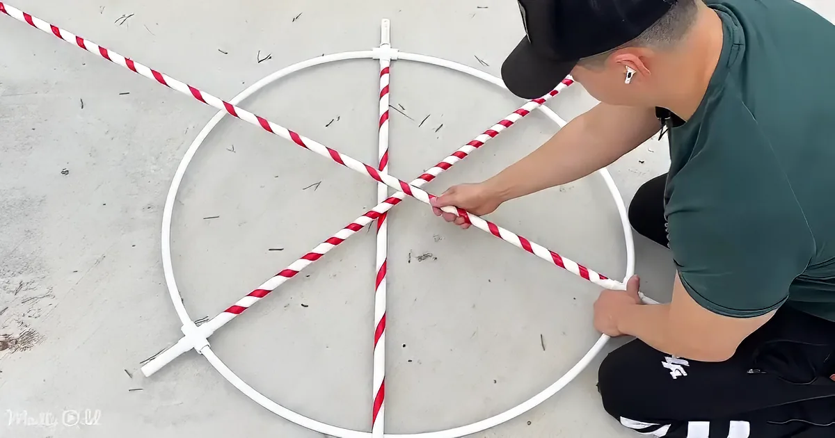 A person is assembling a circular structure using white and red striped poles on a concrete surface.