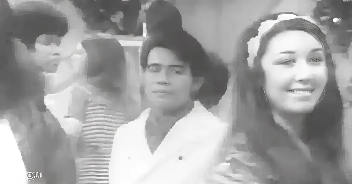 A man in a white shirt stands in a crowd, smiling, with a woman in a dark outfit beside him.