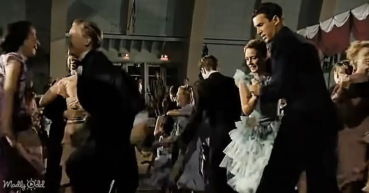 A man in a tuxedo dances with a woman in a white dress at a formal event.