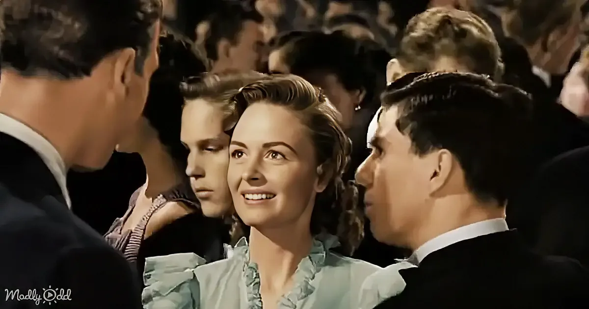 A woman in a light blue dress smiles at a man in a dark suit, surrounded by a crowd in formal attire.
