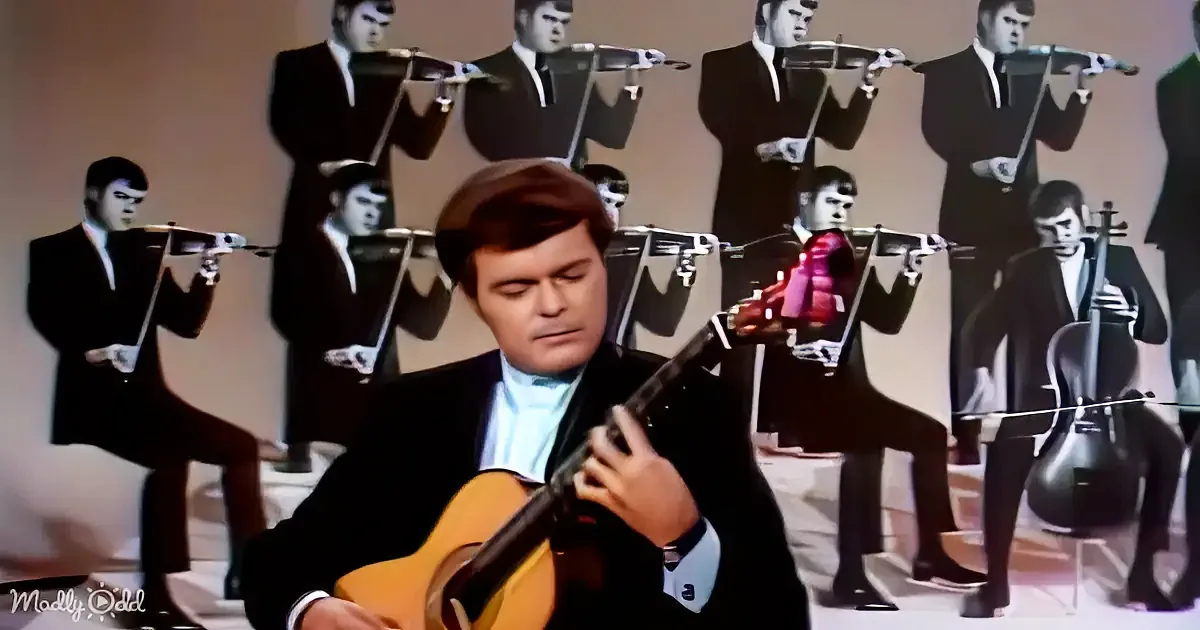 A man in a suit plays a guitar in front of a backdrop of identical violinists.