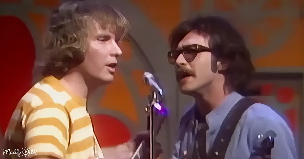 Two musicians, one in a striped shirt, the other in sunglasses, perform on stage with a colorful backdrop.