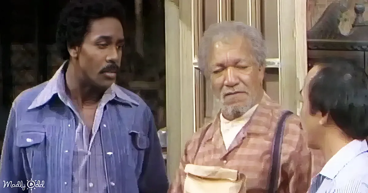 A man in a blue shirt stands beside another man in a checkered shirt, both appearing to be in a conversation.