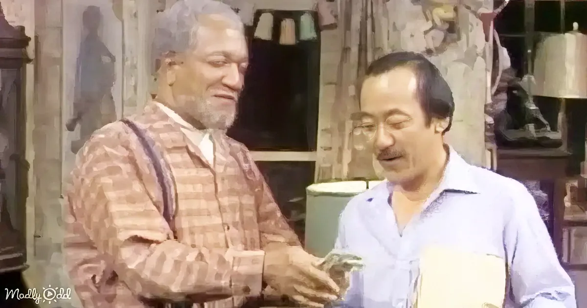 A man in a plaid shirt hands money to another man in a light blue shirt in a cluttered room.