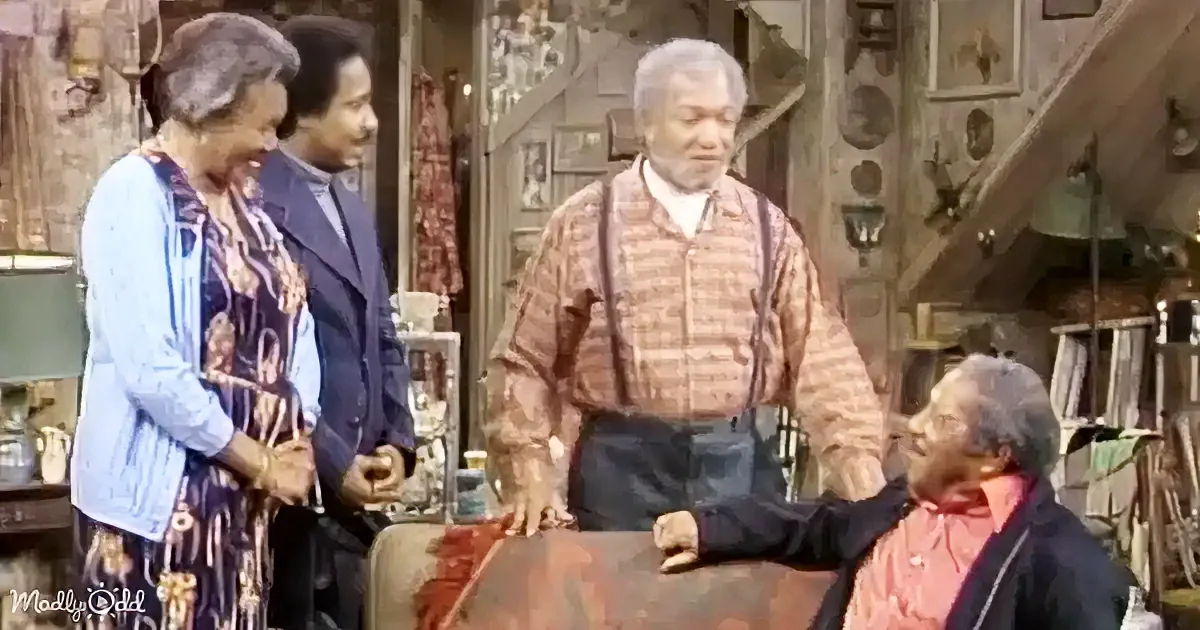 A man in a plaid shirt stands in a cluttered room, surrounded by three other individuals.
