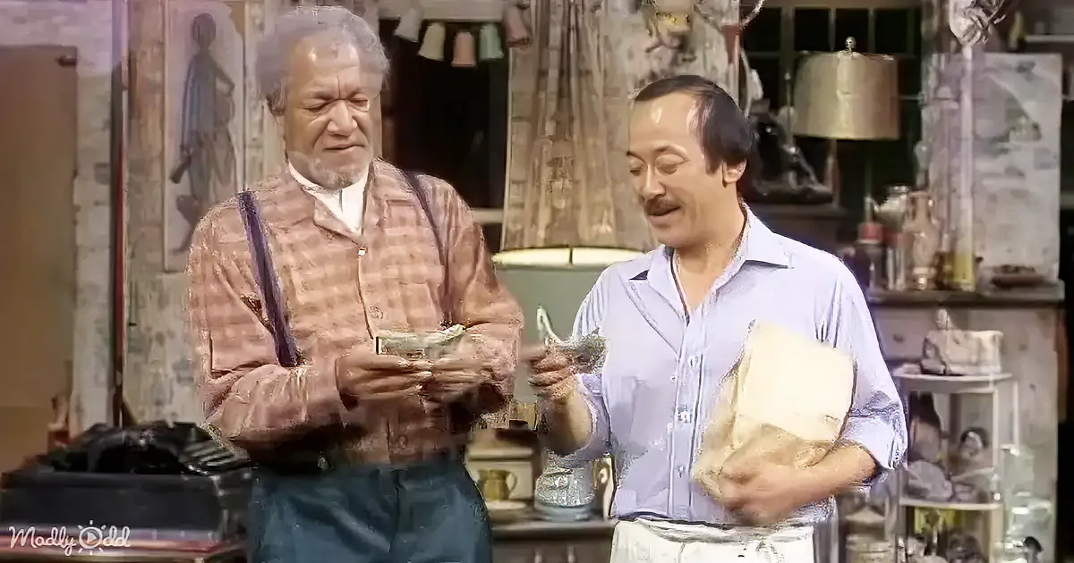 Two men, one holding money and the other a box, stand in a cluttered room with various items around them.