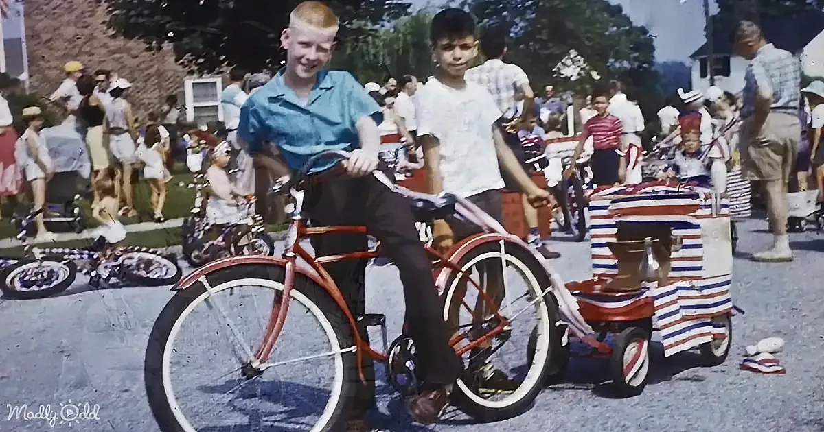 A boy in a blue shirt stands with a red bicycle, surrounded by a crowd of people at an outdoor event.