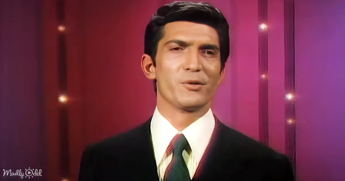 A man in a suit and tie smiles widely, with a red and pink background.