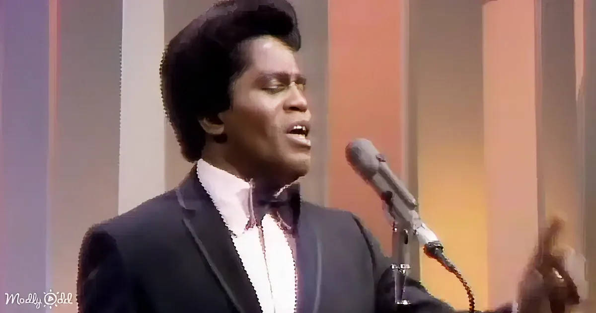 A man in a suit sings into a microphone on stage, wearing glasses and a bow tie.