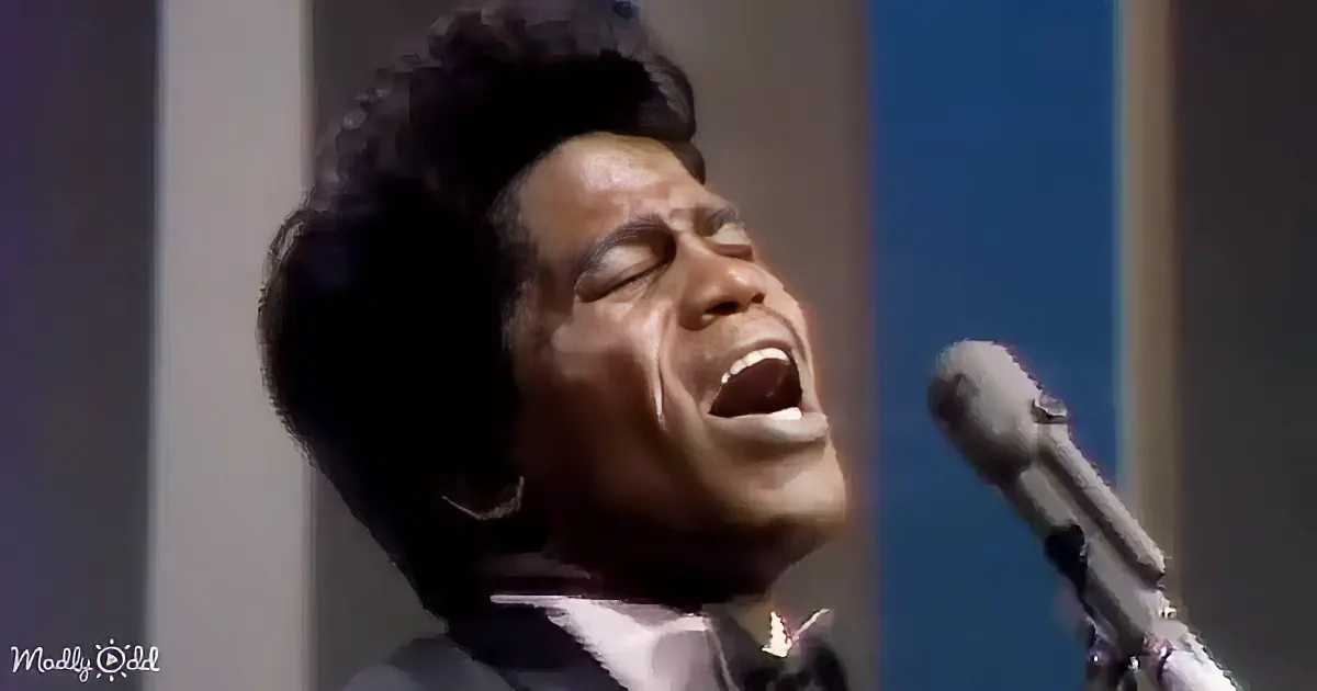 A man in a suit sings into a microphone on a stage with colorful vertical stripes.