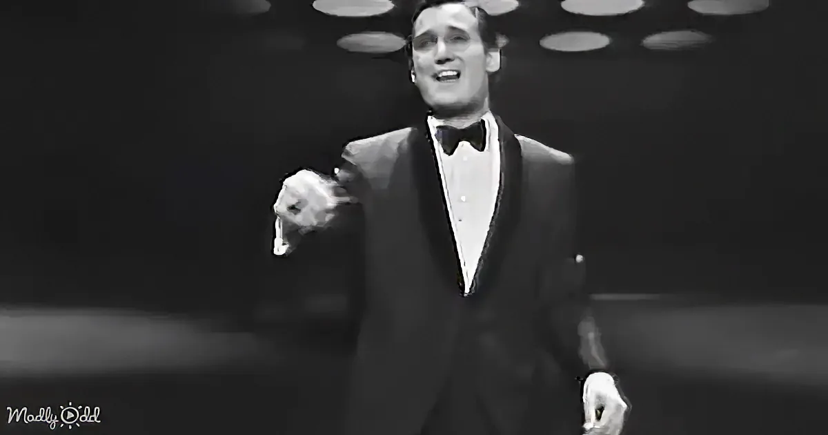 A man in a tuxedo and bow tie is dancing on stage, holding a microphone.